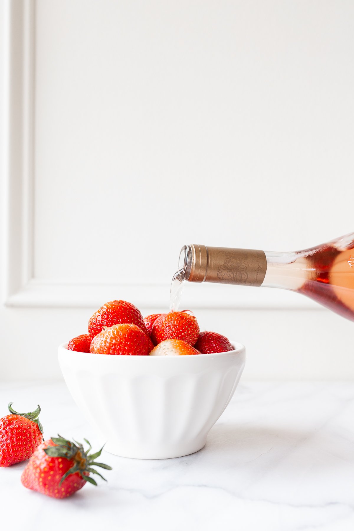rosé marinated drunken strawberries in a white bowl, bottle of wine pouring over the top