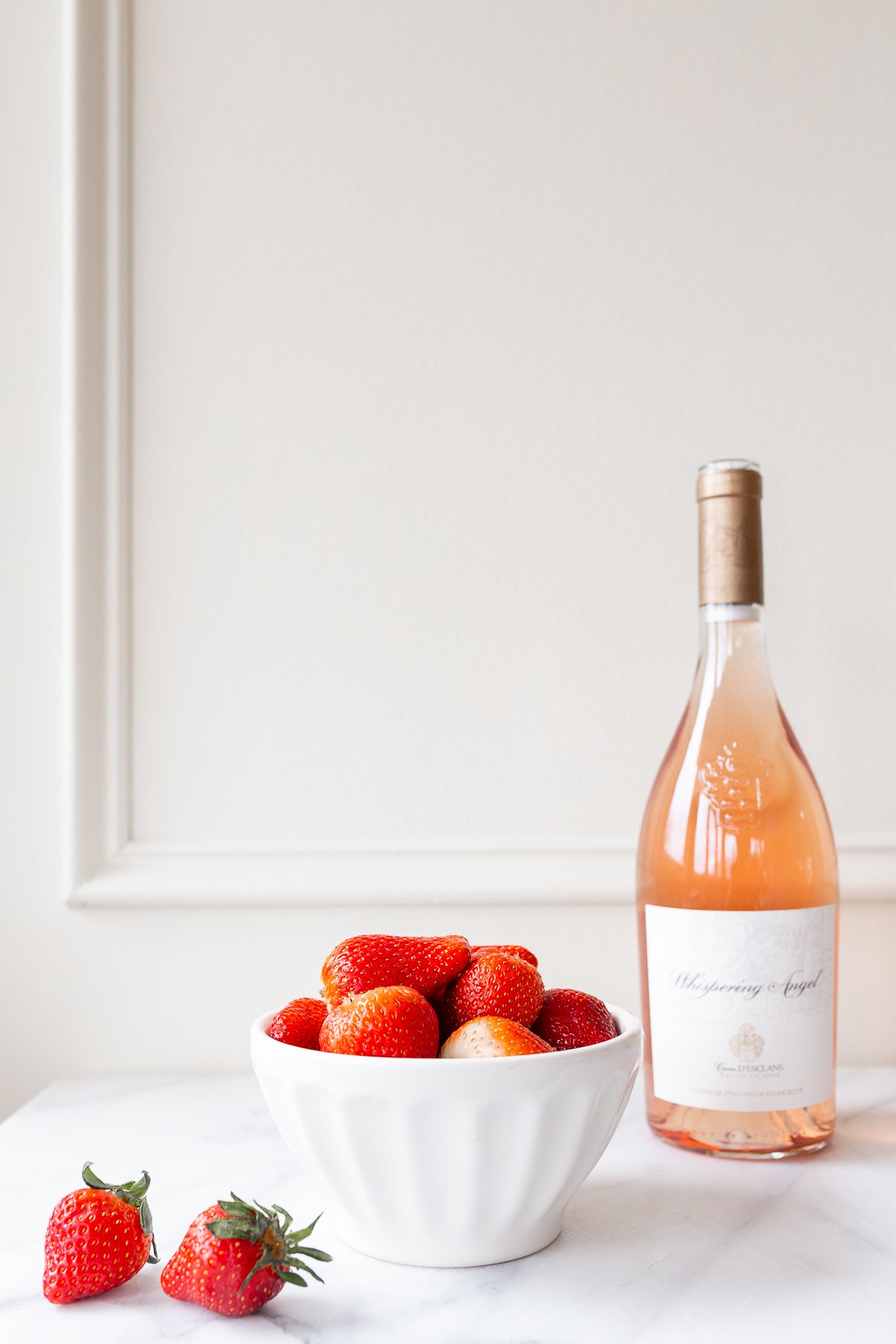rosé marinated drunken strawberries in a white bowl, bottle of wine in the background.