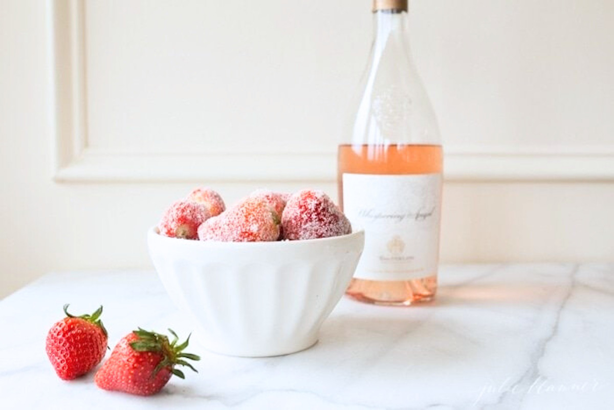 rosé marinated drunken strawberries in a white bowl, bottle of wine in the background.