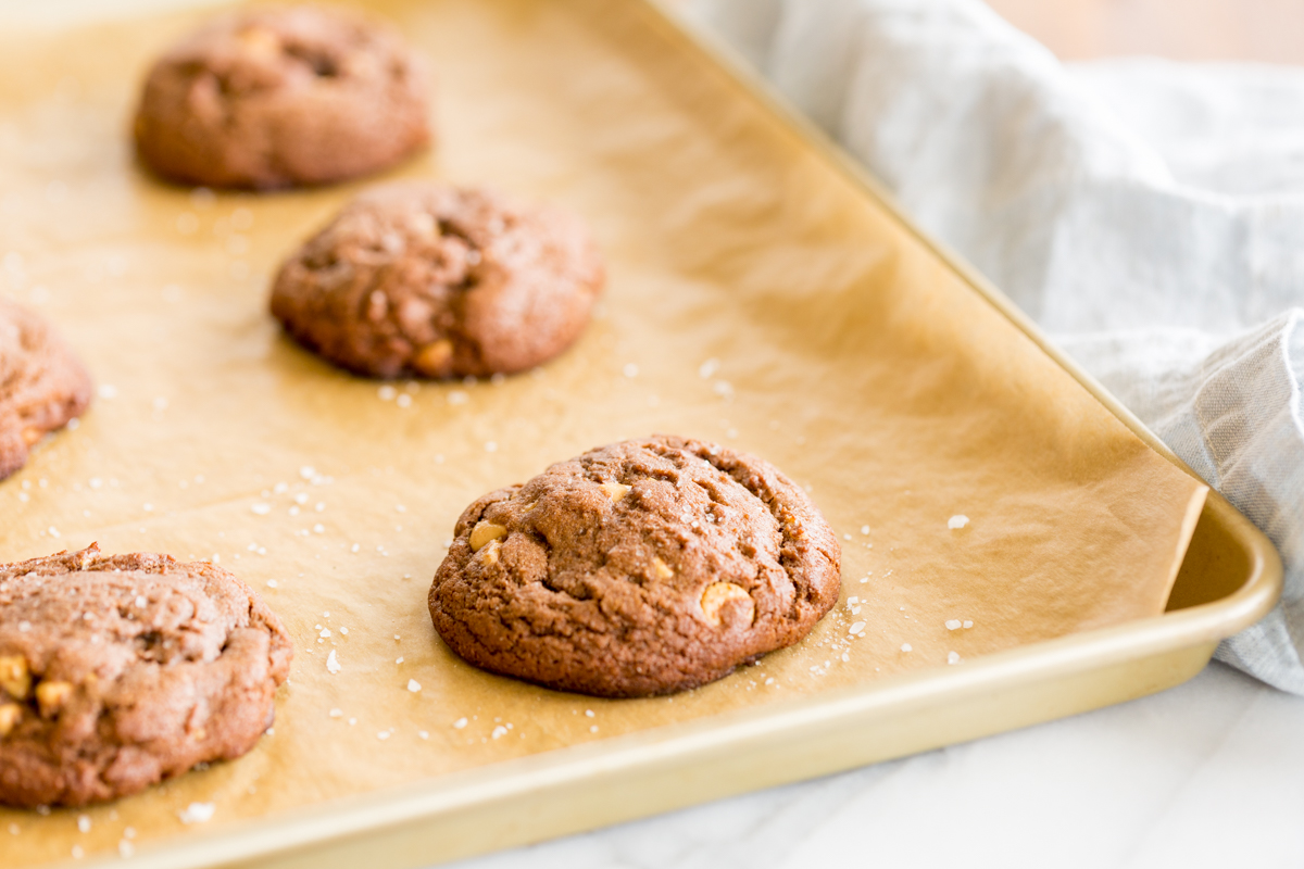 A gold baking tray lined with parchment, full of chocolate cookies with peanut butter chips.