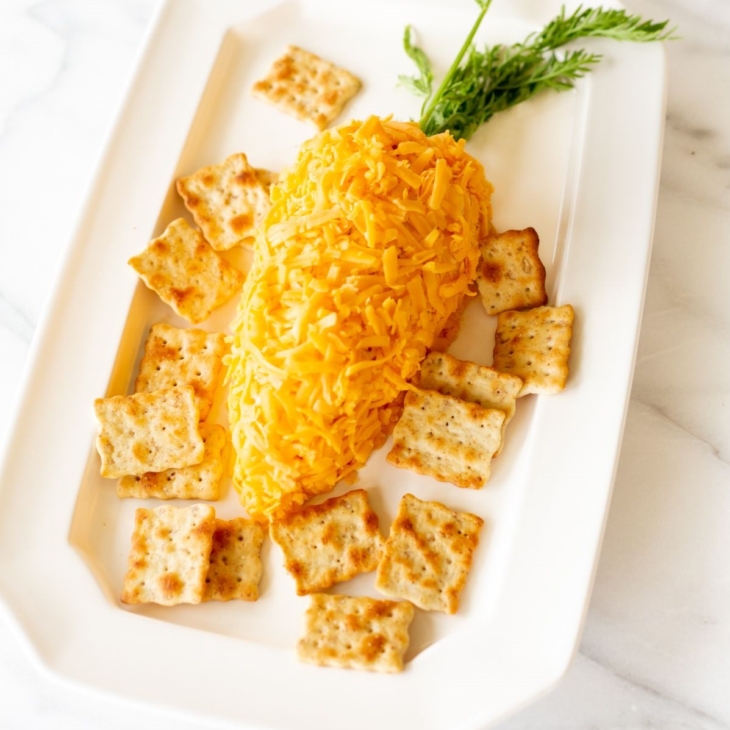 A carrot shaped cheese ball on a white plate, surrounded by crackers.