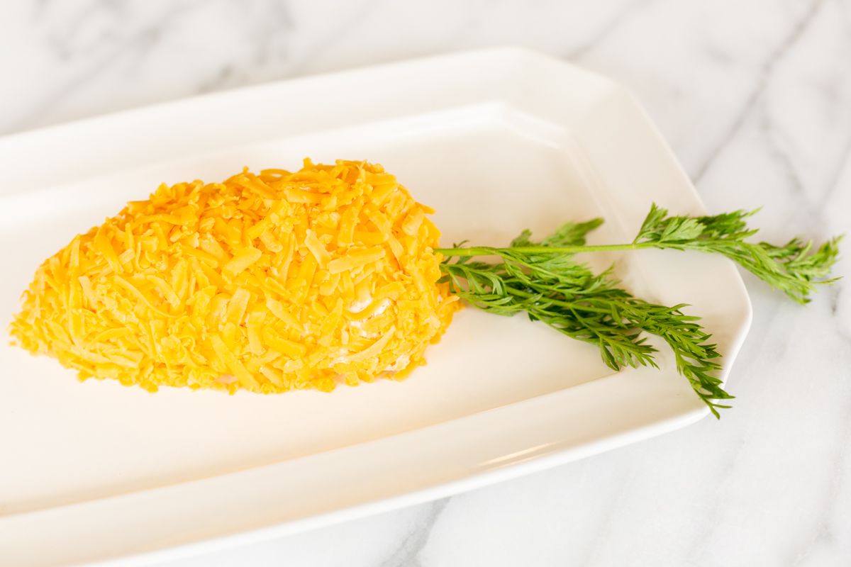 A carrot cheese ball on a white platter.