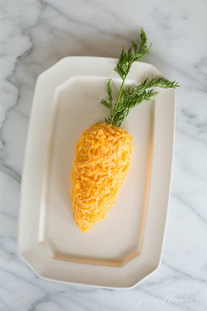 A white platter with a cheeseball in the shape of a carrot for Easter