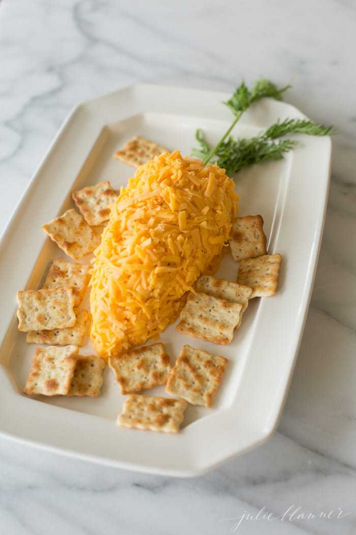 A carrot cheeseball on a white platter surrounded by crackers