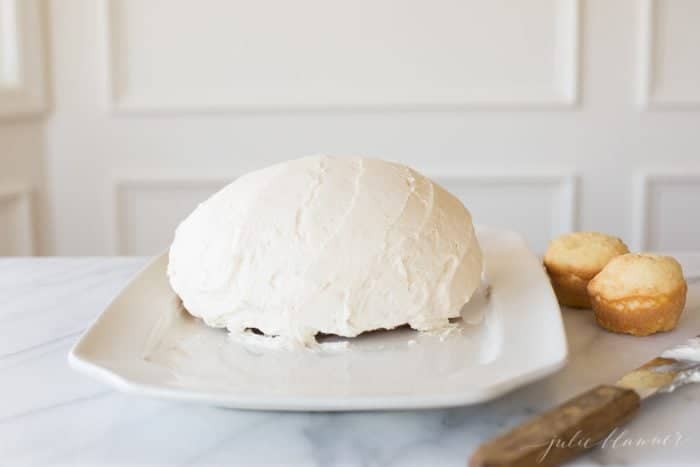 A round cake frosted in white frosting on a white platter to make an Easter Bunny Cake.