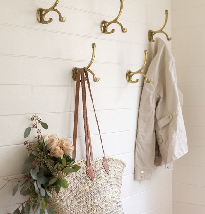 a mudroom with white horizontal paneling and brass coat hooks