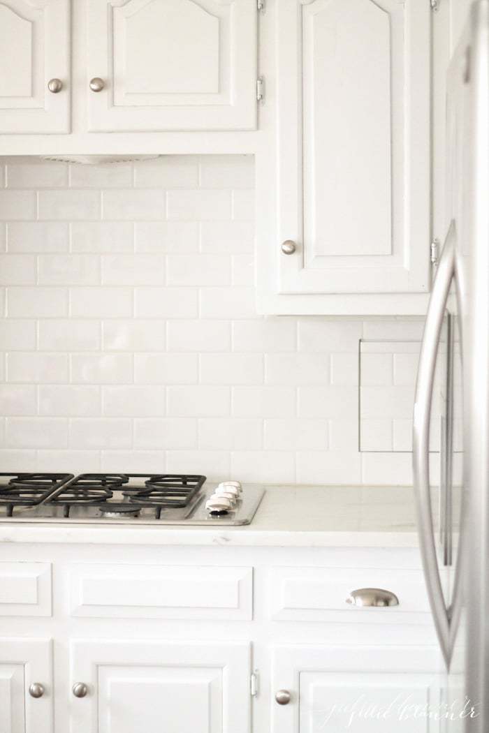 A kitchen with painted white cabinets and marble countertops