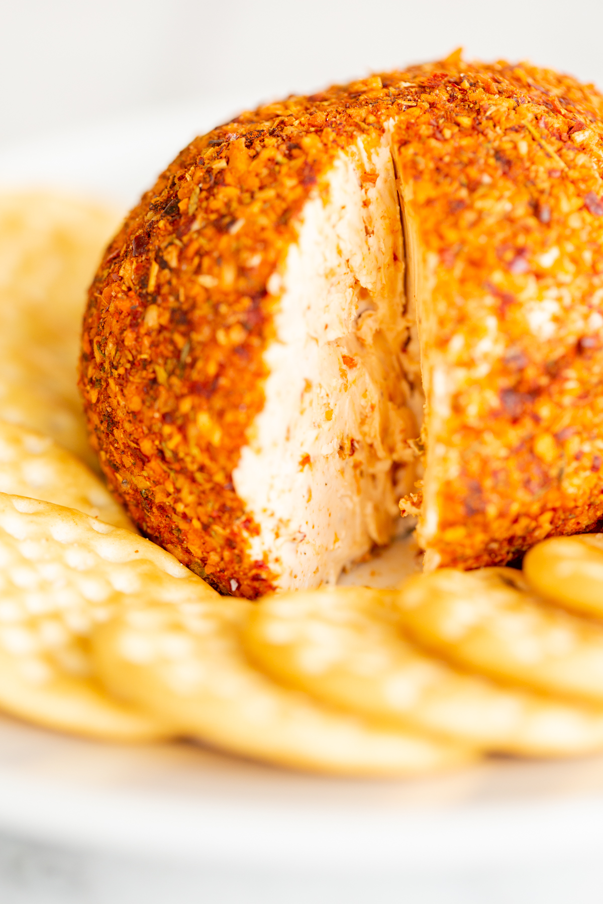 A spicy cheese ball on a white plate surrounded by crackers.