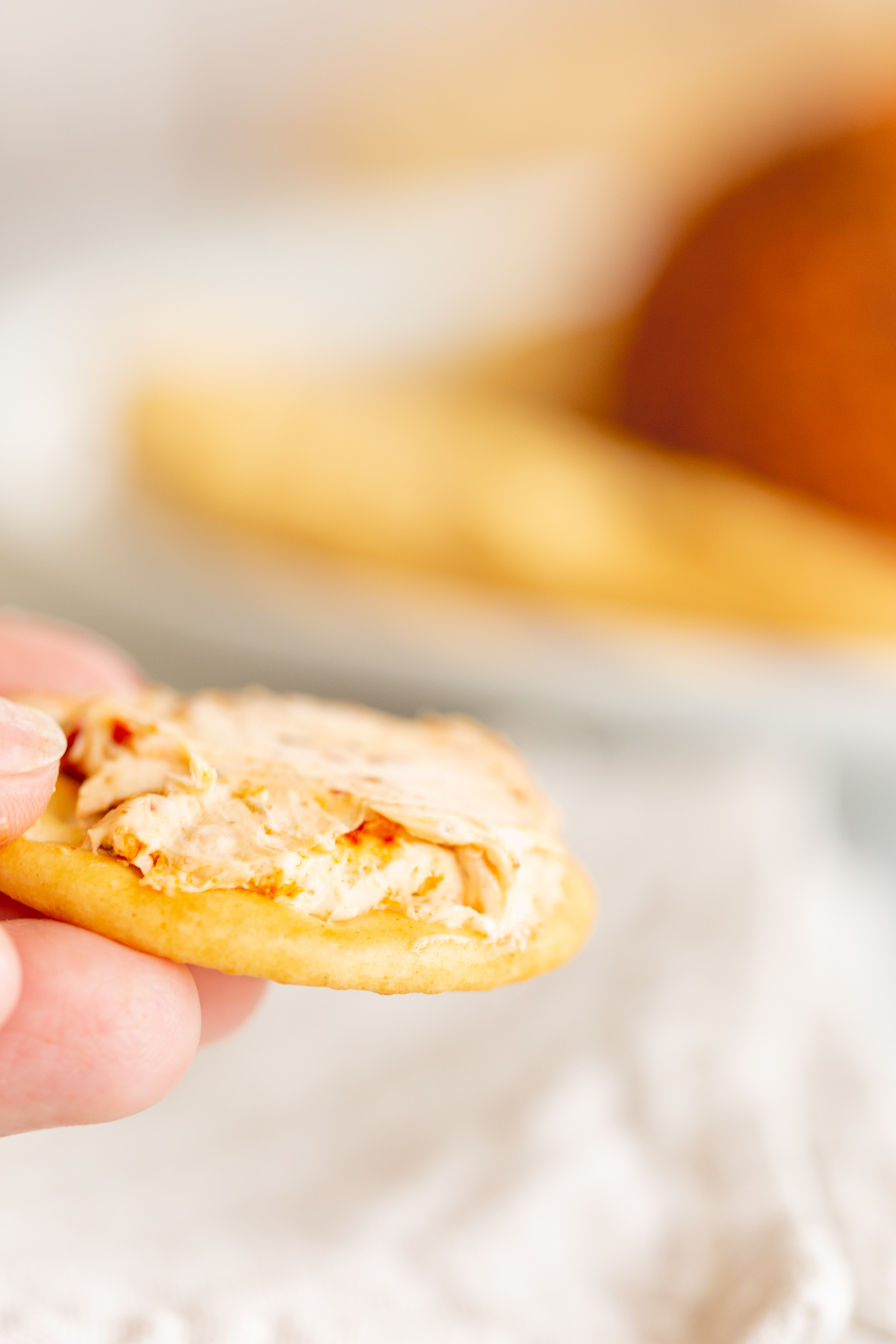 A hand holding a cracker topped with a spread from a spicy cheeseball.