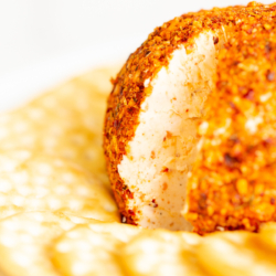 A spicy cheese ball on a white plate surrounded by crackers.