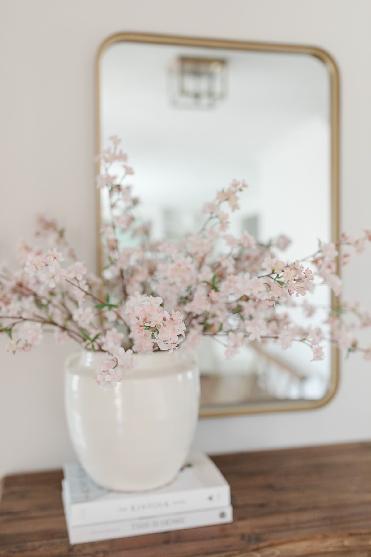 Faux flowers in a white vase in front of a gold mirror