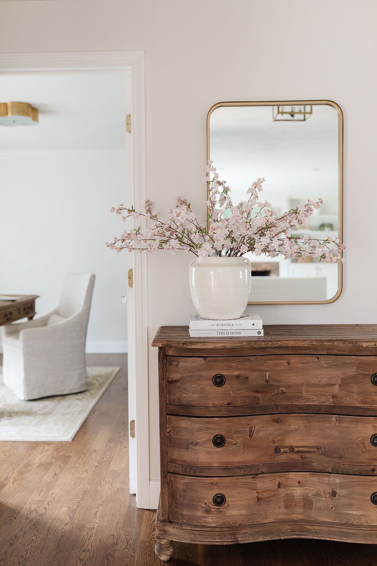 Faux flowers in a white vase in front of a gold mirror