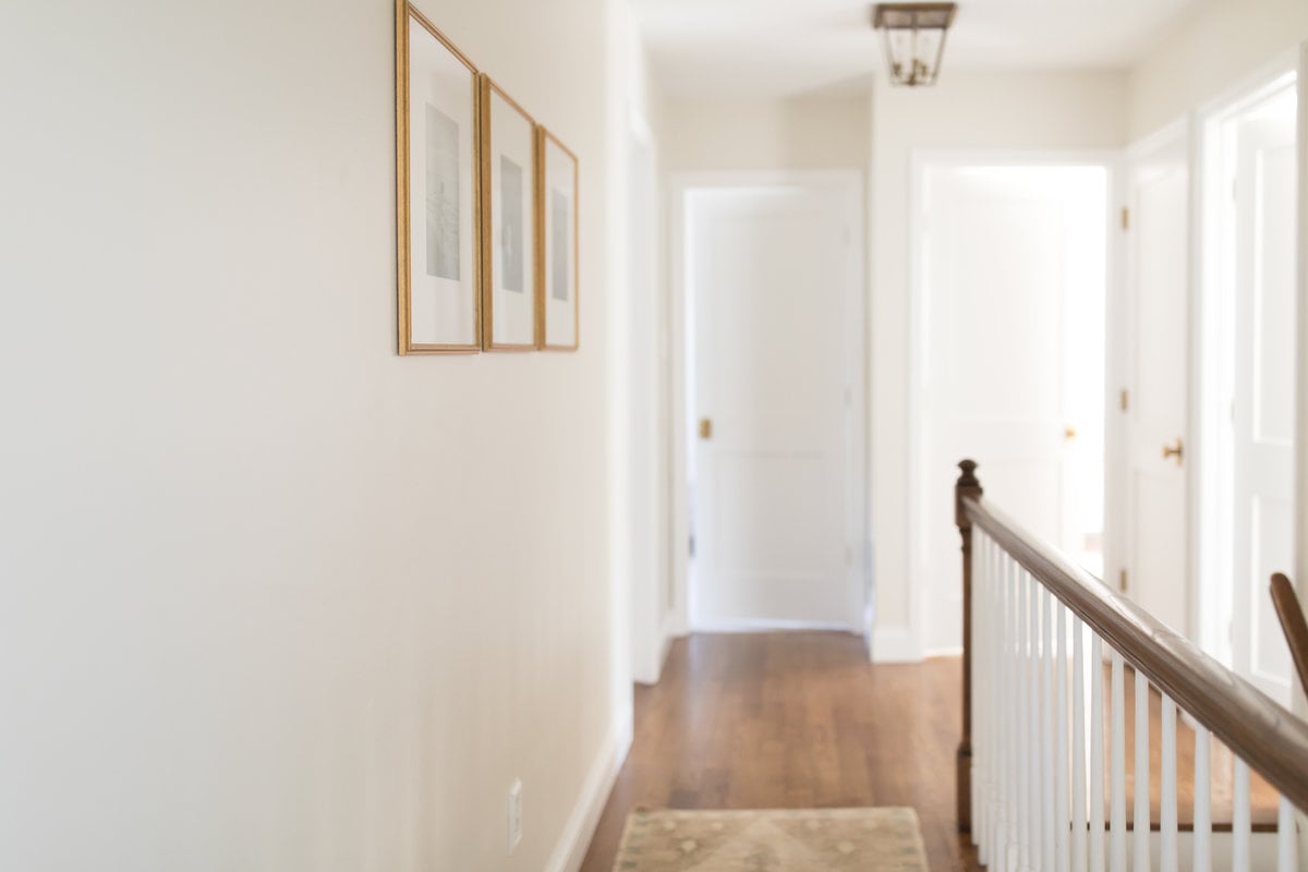 A hallway with white walls, wood floors and flush mount lanterns in a brass finish.