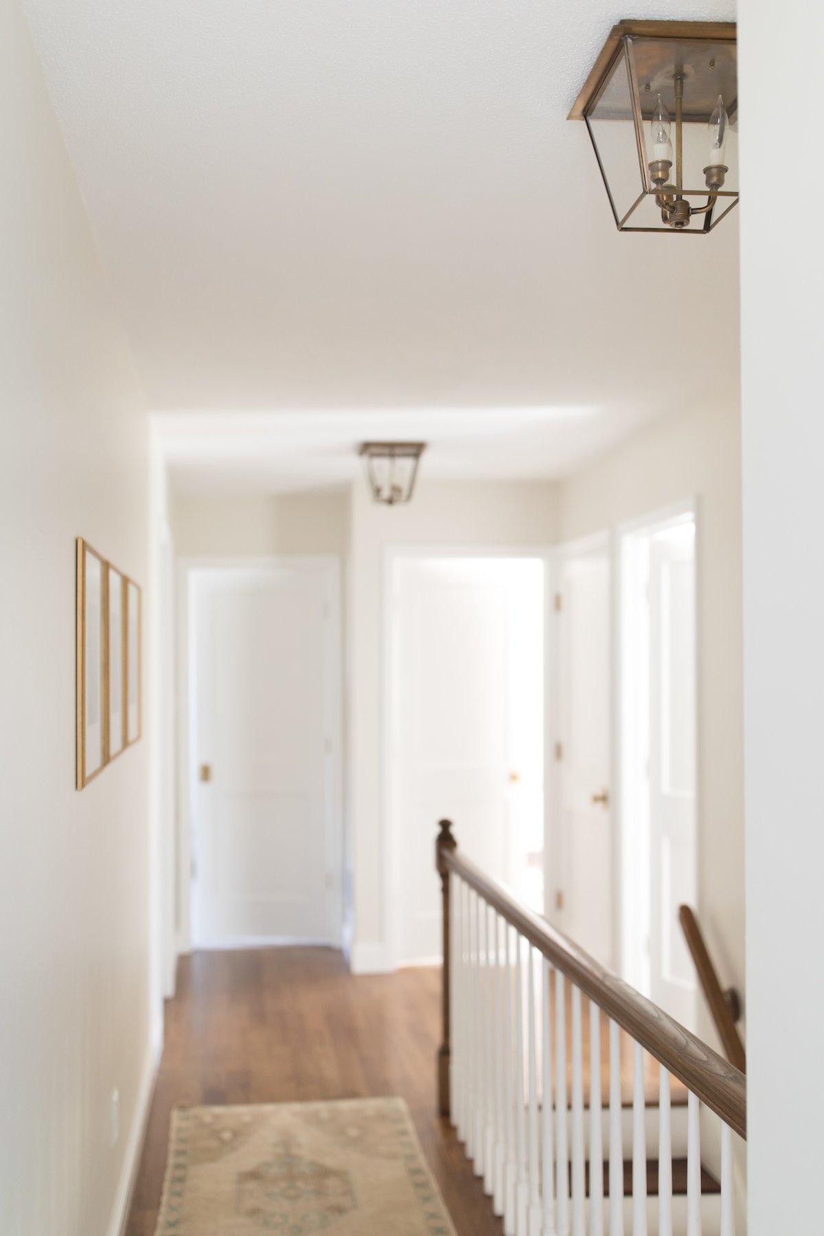 A hallway with white walls, wood floors and flush mount lanterns in a brass finish. 