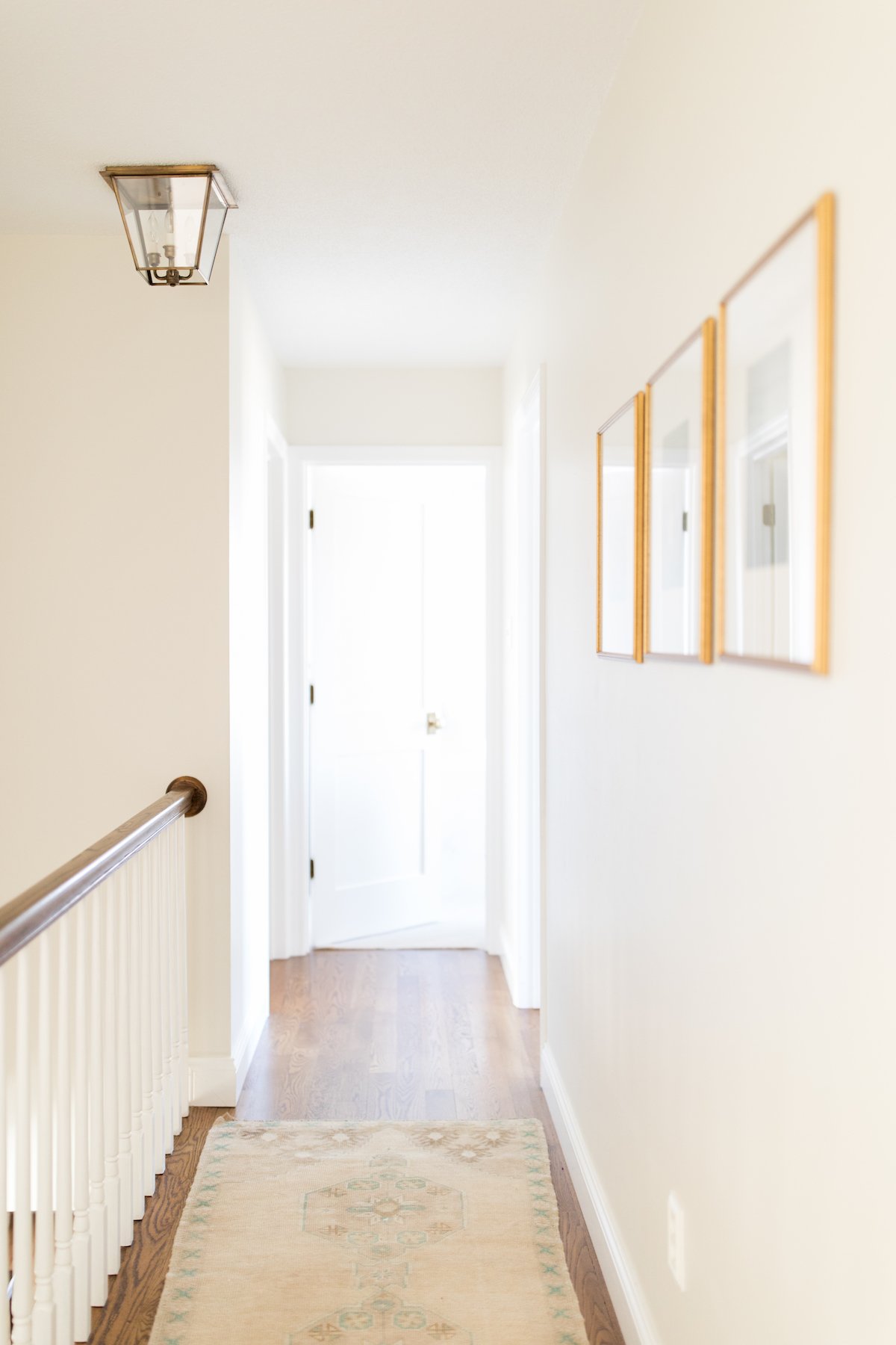 A hallway with white walls, wood floors and flush mount lanterns in a brass finish.