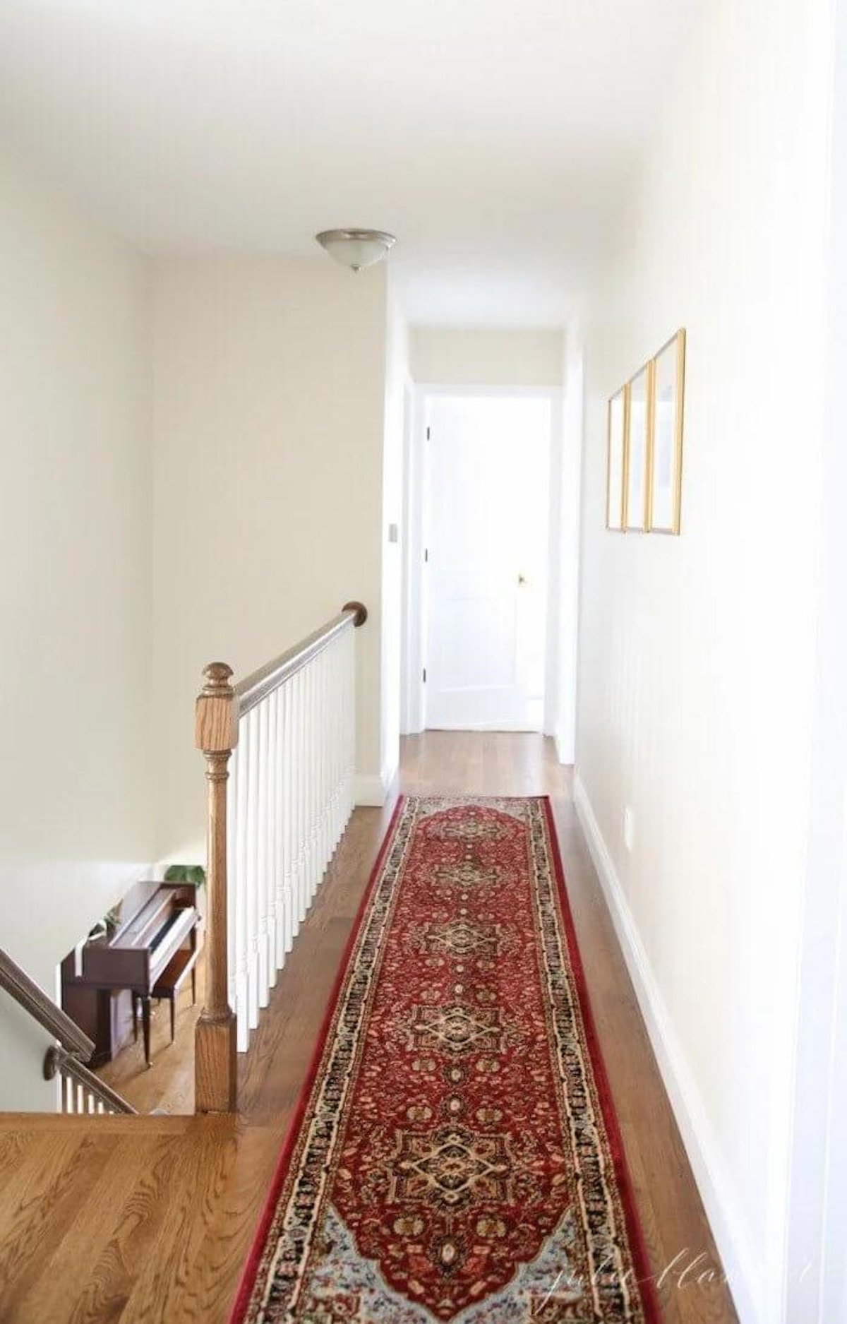 A hallway with white walls, a red rug, and a dated flush mount light fixture. 