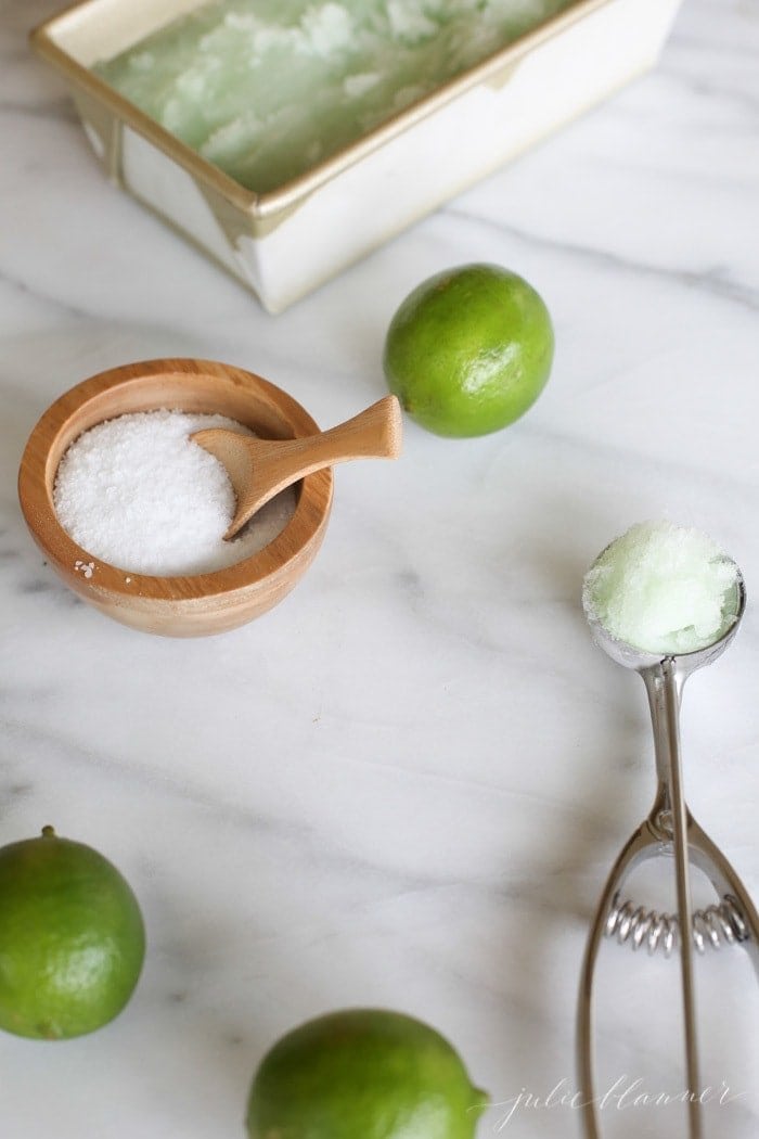 limes next to lime sorbet in an ice cream scoop and bowl of sea salt