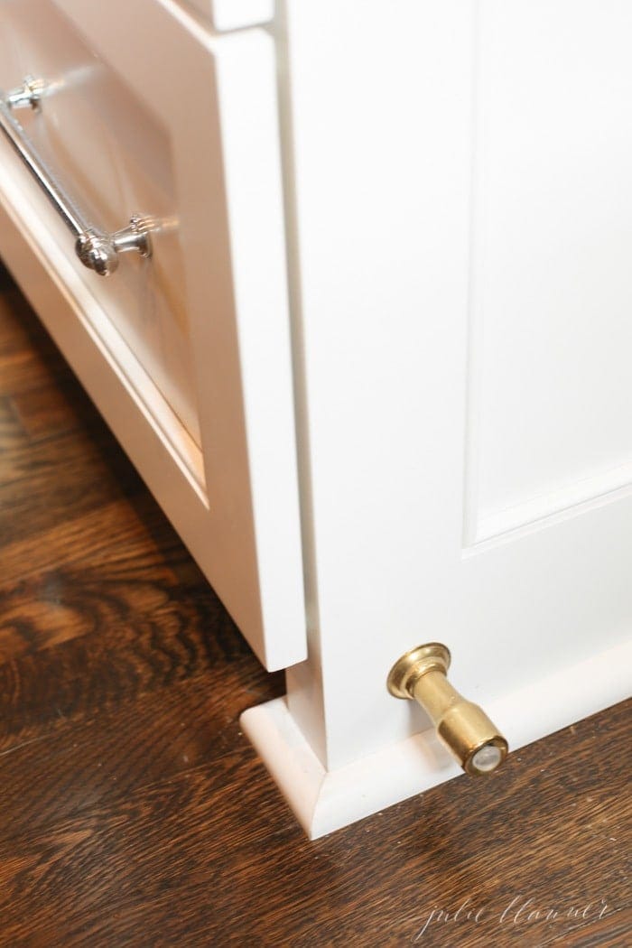A brass doorstop in a white kitchen with wood floors