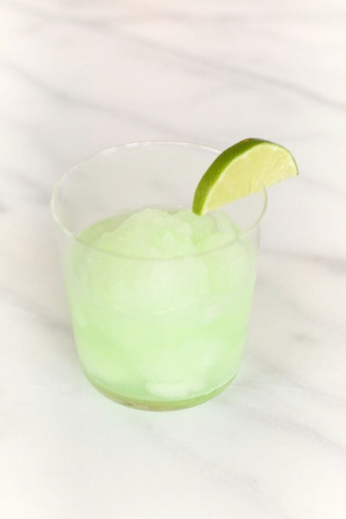 A glass filled with light green, shaved ice garnished with a slice of lime on the rim, creating a refreshing margarita float.