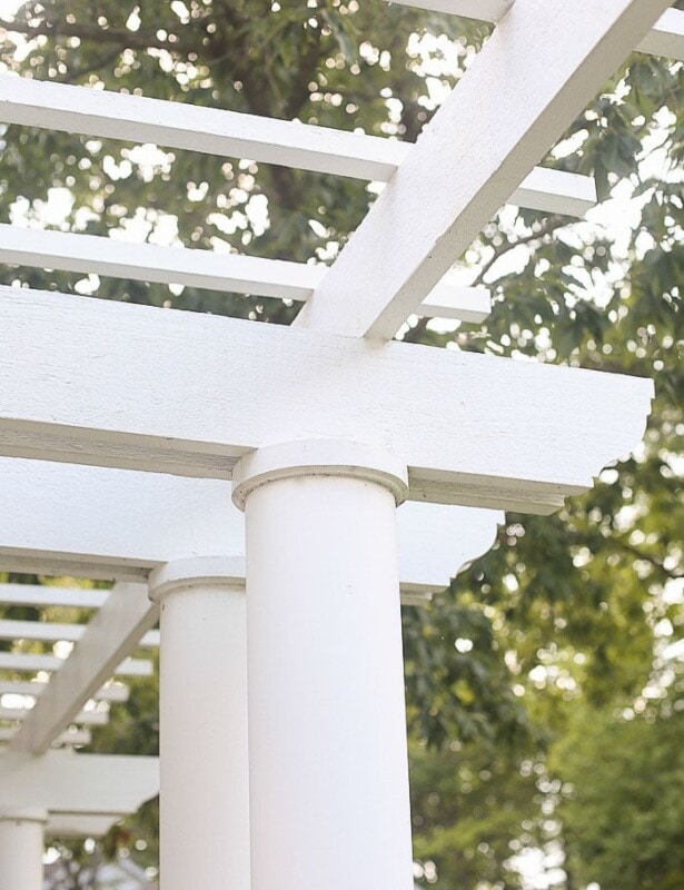A white pergola attached to house with a tree in the background