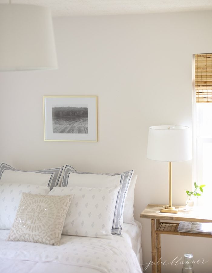 Looking inside a white bedroom with a black and white photo on the wall over the bed.