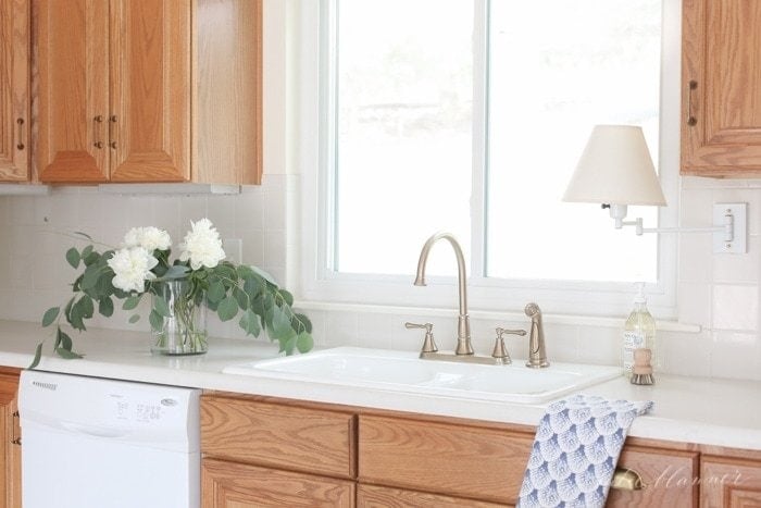 closeup of 90s kitchen with oak cabinets, champagne bronze faucet, brass cabinet hardware, and white porcelain sink