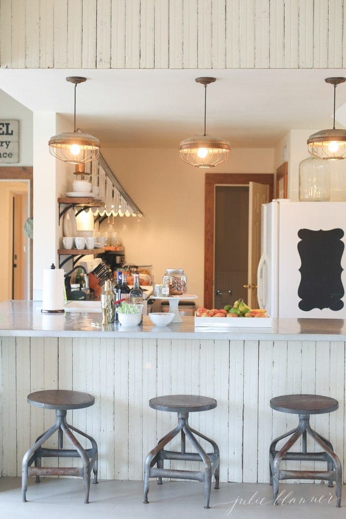 Rustic industrial farmhouse kitchen with three charming light pendants and industrial stools at the bar.
