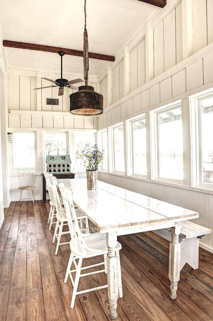 A rustic white industrial farmhouse dining room with a long farm table.