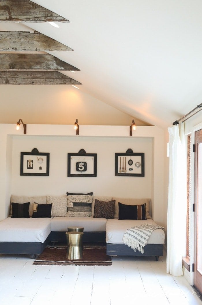 A farmhouse living room with raw wood barn inspired beams, white walls and vintage furnishings.