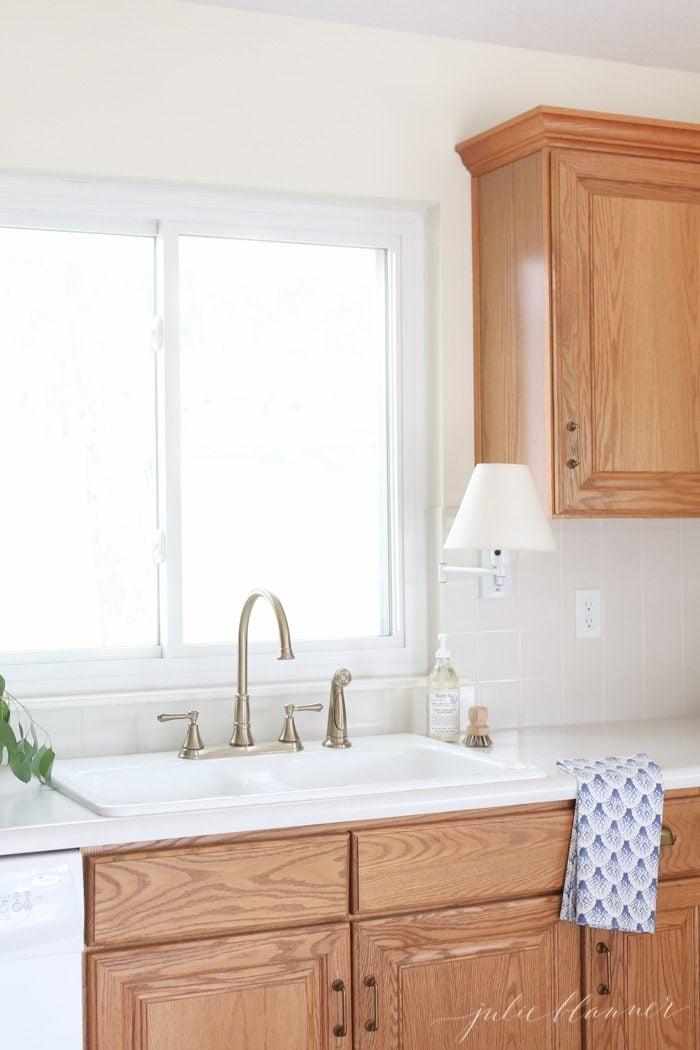 Scalloped blue and white dish cloth on counter near porcelain sink. Accents are a simple way to update a kitchen with oak cabinets.