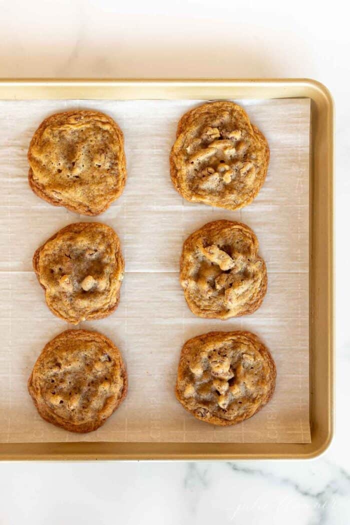 A gold baking sheet lined with parchment paper and six pecan pie cookies.