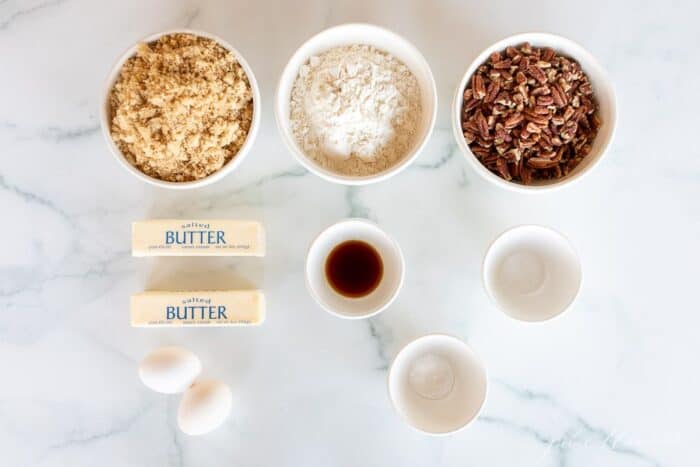 A marble surface with ingredients for butter pecan pie cookies laid out in small white bowls.