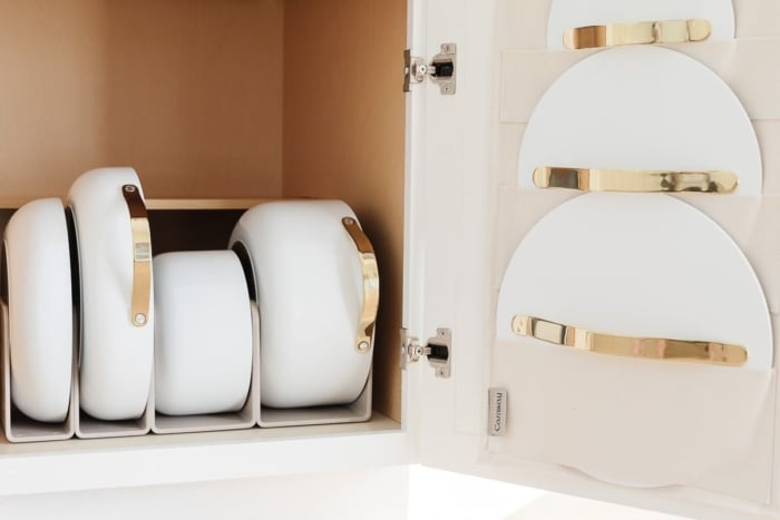 Caraway cookware in a white kitchen cabinet, with pot lid storage on the interior of the cabinet door.