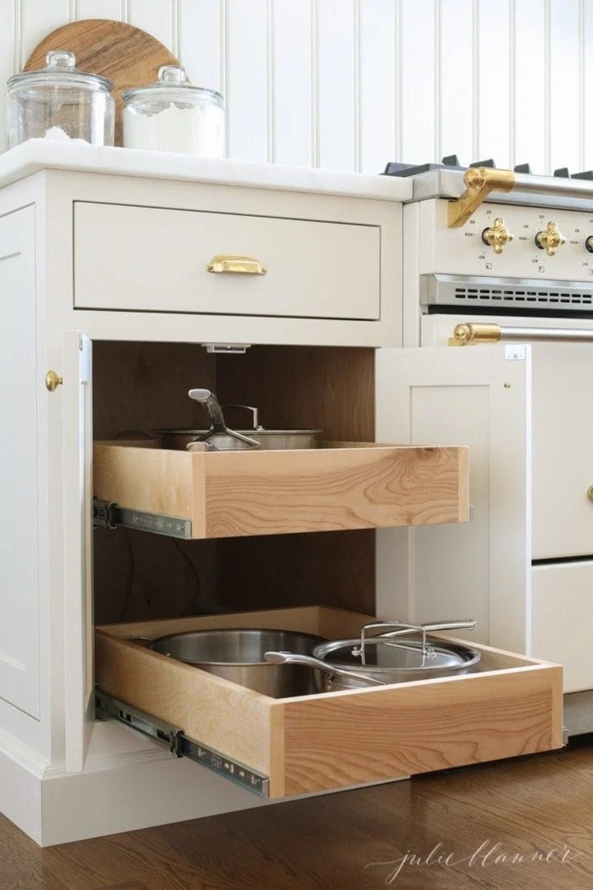 Pull out drawers for pots and pans storage in a kitchen cabinet by a French range.