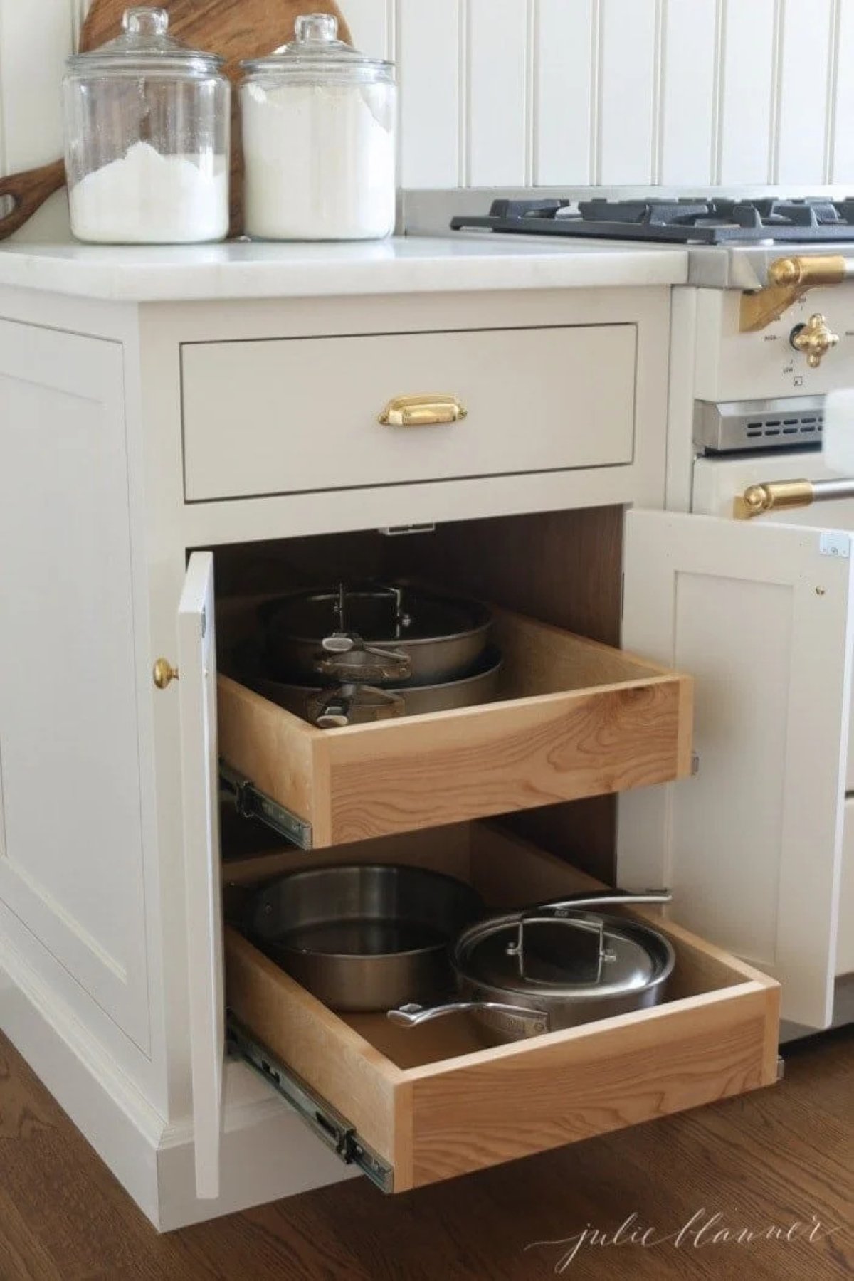 Pull out drawers for pots and pans storage in a kitchen cabinet by a French range.
