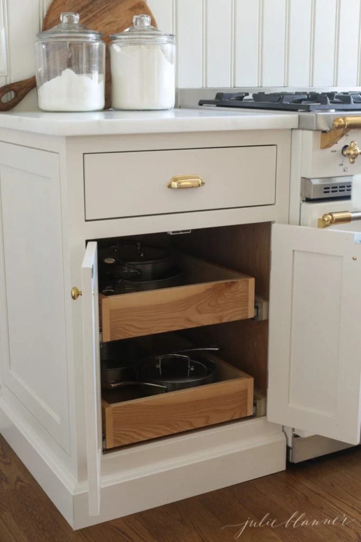 Pull out drawers for pots and pans storage in a kitchen cabinet by a French range.