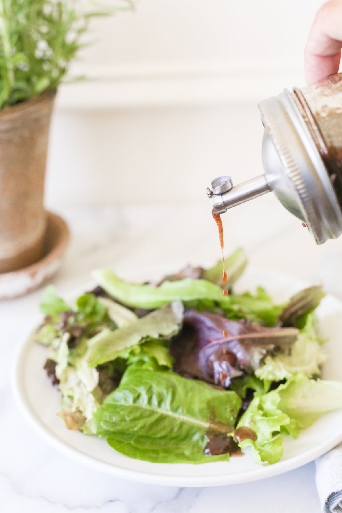 Balsamic vinaigrette in a glass bottle, pouring over a salad.
