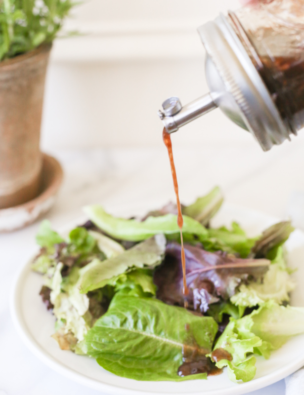 Balsamic vinaigrette in a glass bottle, pouring over a salad.