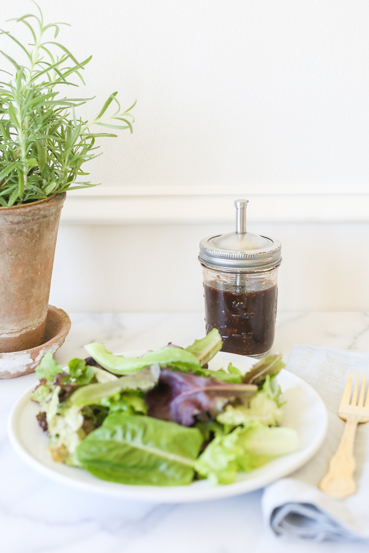 Balsamic vinaigrette in a glass bottle, next to a plate of salad.