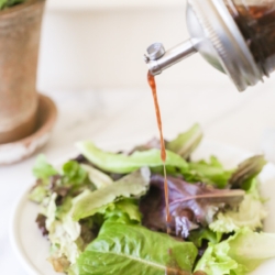 Balsamic vinaigrette in a glass bottle, pouring over a salad.