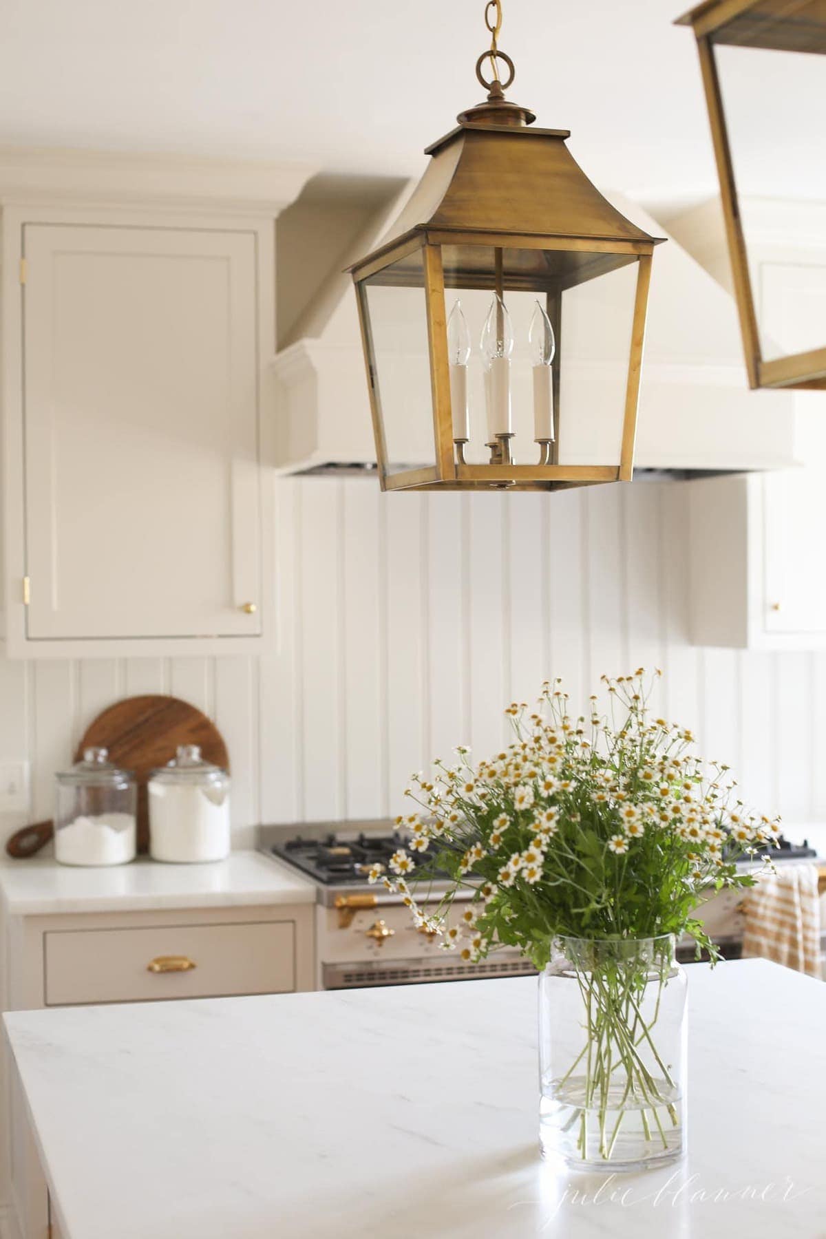 A cream kitchen with marble countertops and a vase of flowers on the island.