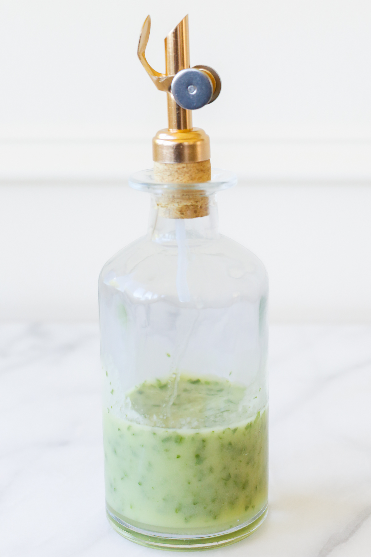 A clear glass bottle of a green herb vinaigrette.