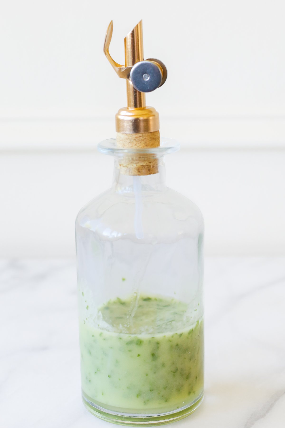 A clear glass bottle of a green herb vinaigrette.