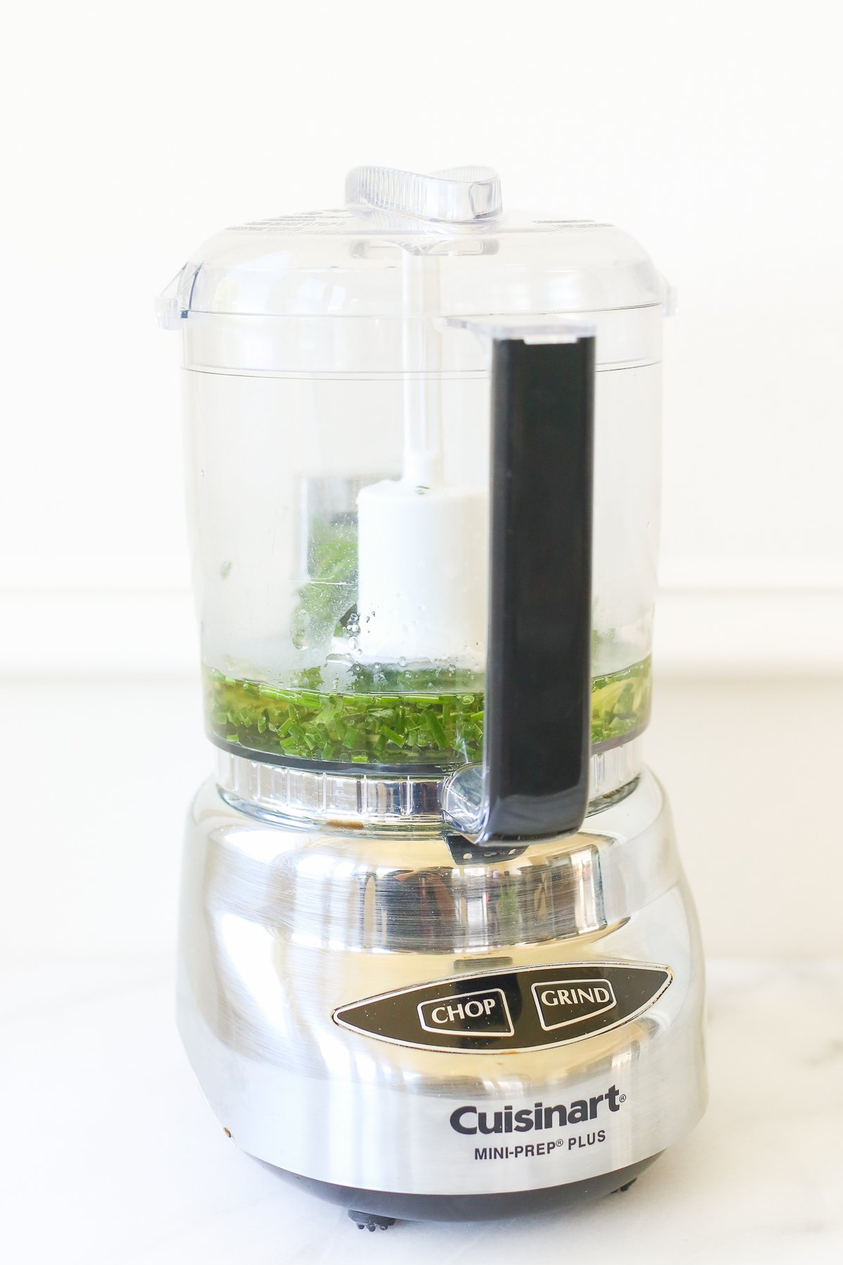 A stainless steel food processor with fresh herbs chopped in the bowl.