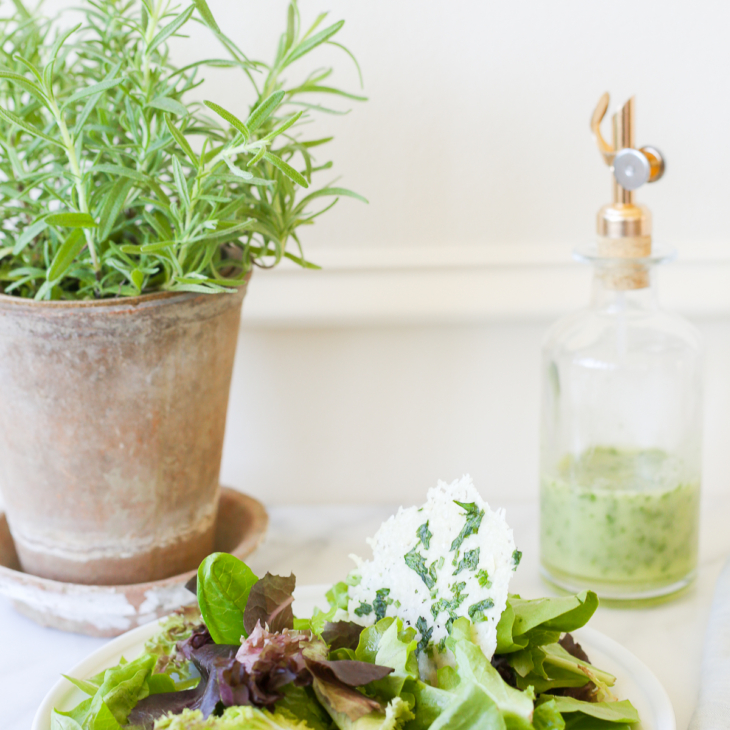 A leafy green salad on a white plate, with a glass bottle of herb vinaigrette in the background.
