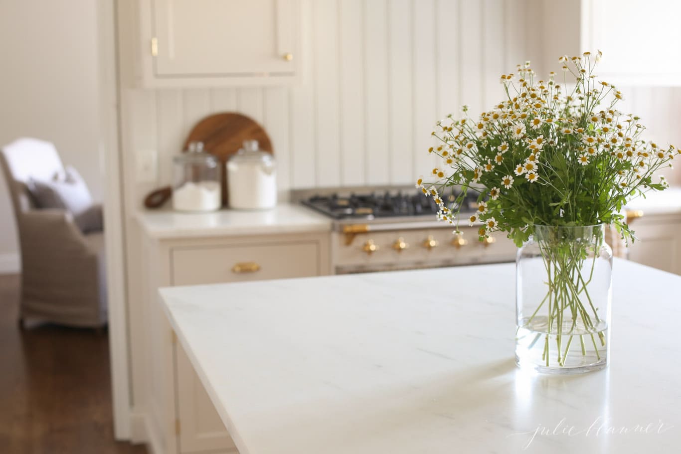 A cream kitchen with marble countertops and a vase of flowers on the island.