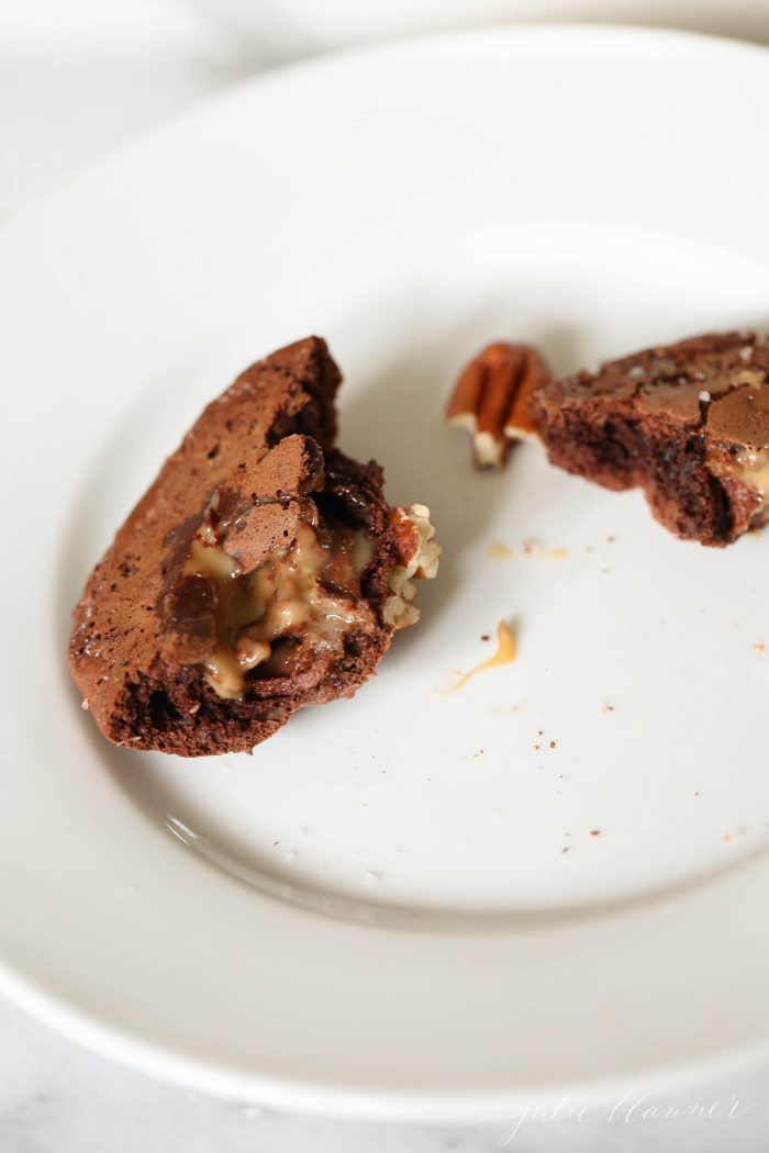 A chocolate turtle cookie broken in half on a white plate