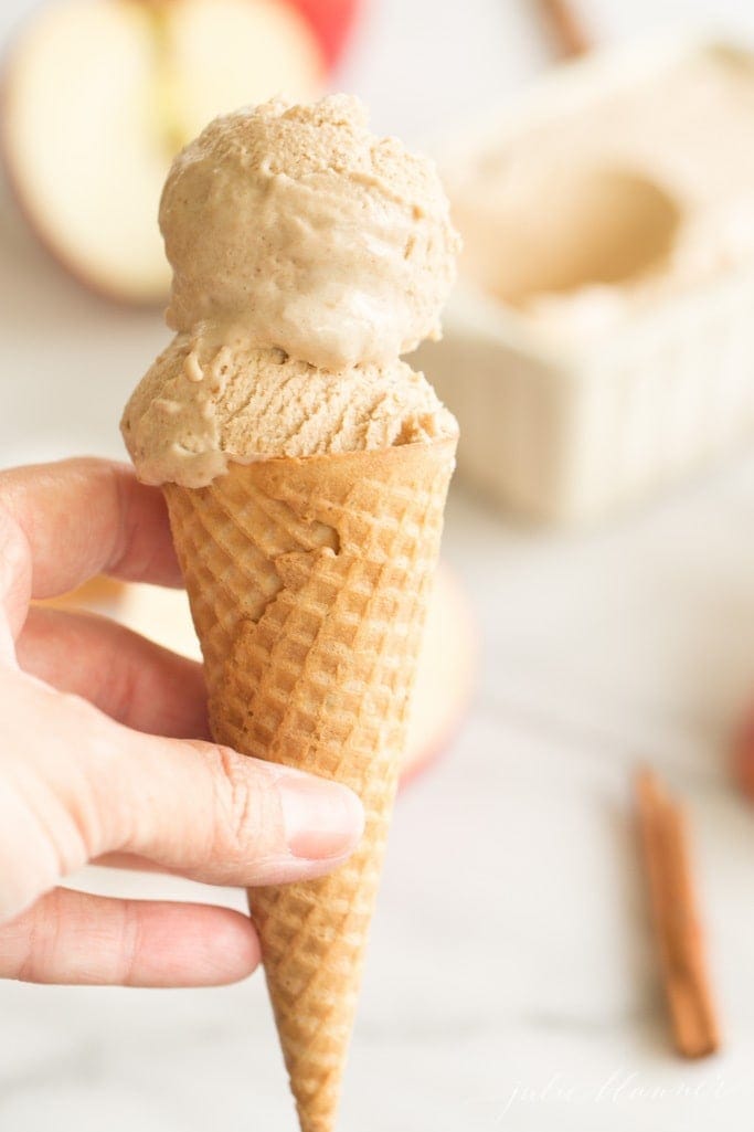 creamy apple butter ice cream scoops in a waffle cone, held by a hand on the left
