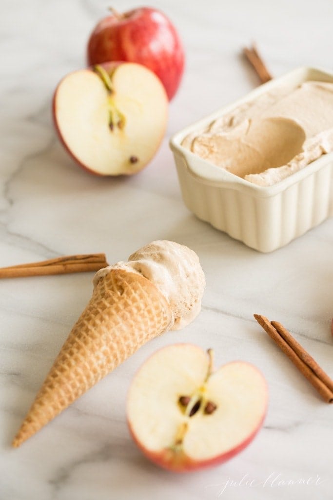 Apple butter ice cream in a loaf pan, with a cone full of ice cream and sliced apples in the foreground.
