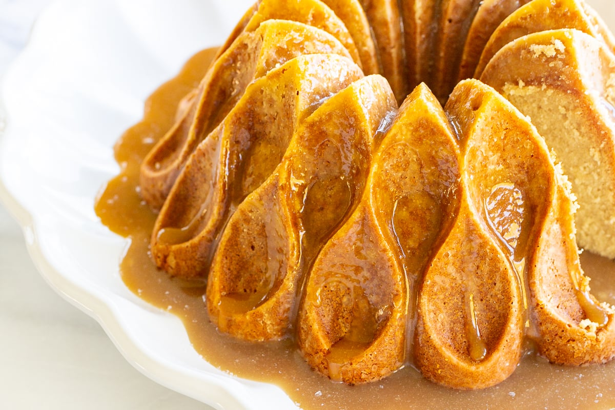 A brown sugar caramel pound cake on a white platter, baked in a bundt pan and topped with caramel sauce.